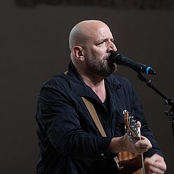 ein Mann mit Gitarre und Mikrofon vor einem Mikrofon