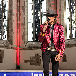 ein Mann in einer roten Jacke und Hut singen in ein Mikrofon