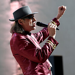 ein Mann in einem rosa Anzug und Hut singen in ein Mikrofon